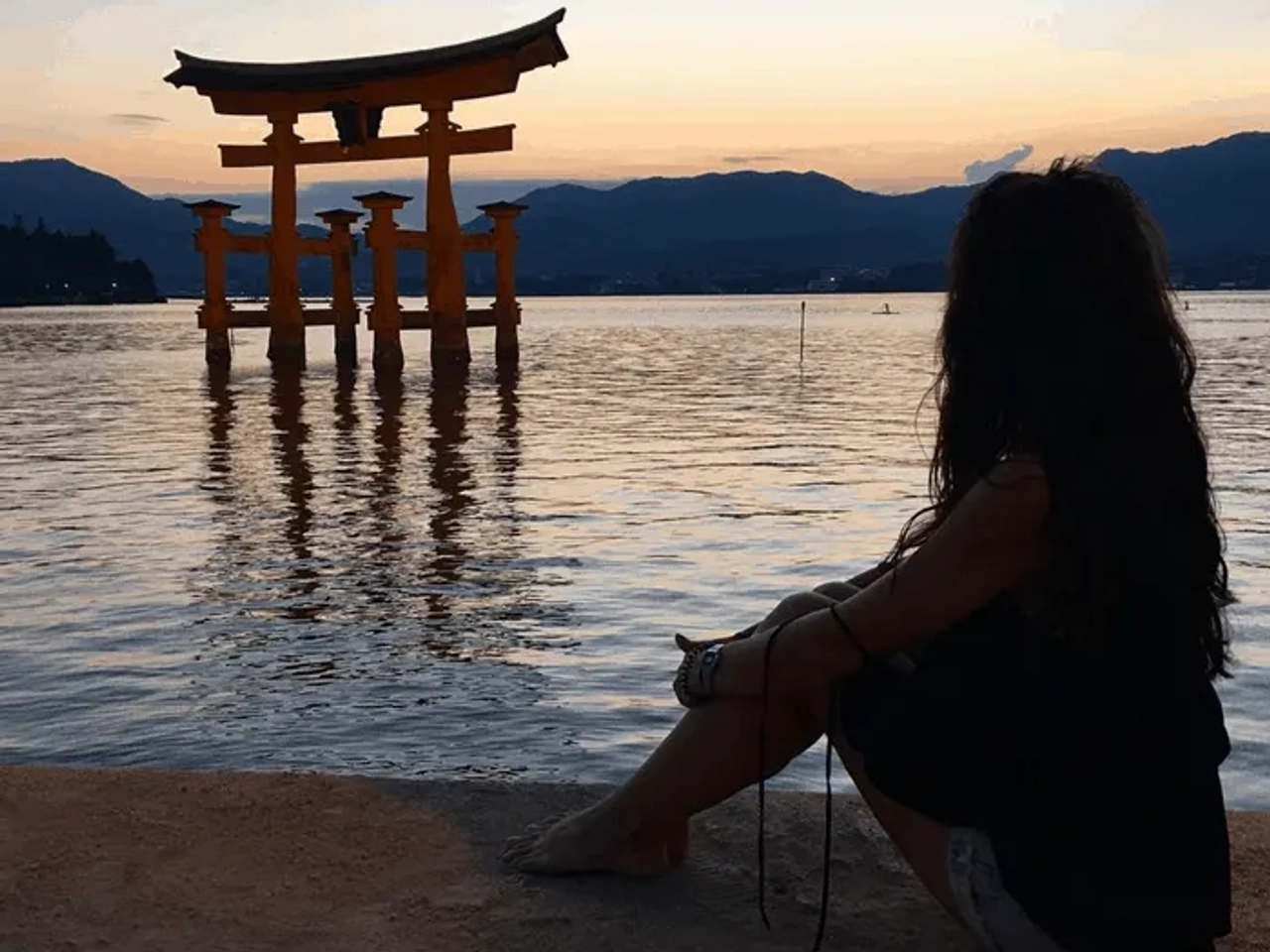 Mujer contemplando un torii en el agua durante el atardecer.