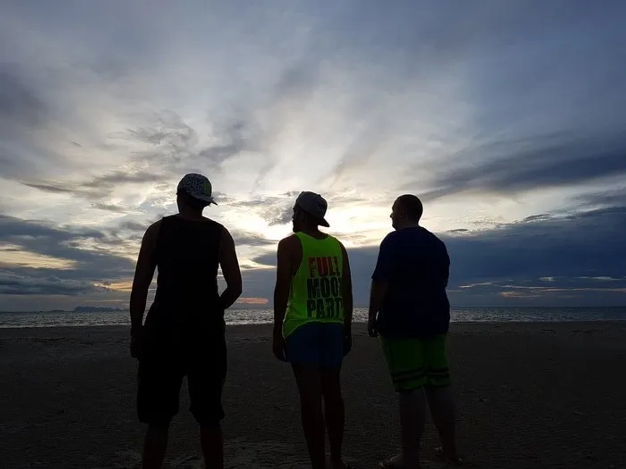Tres personas de espaldas contemplan un atardecer en la playa.