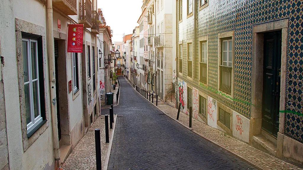 Rua estreita em Lisboa, com fachadas coloridas e azulejos típicos.