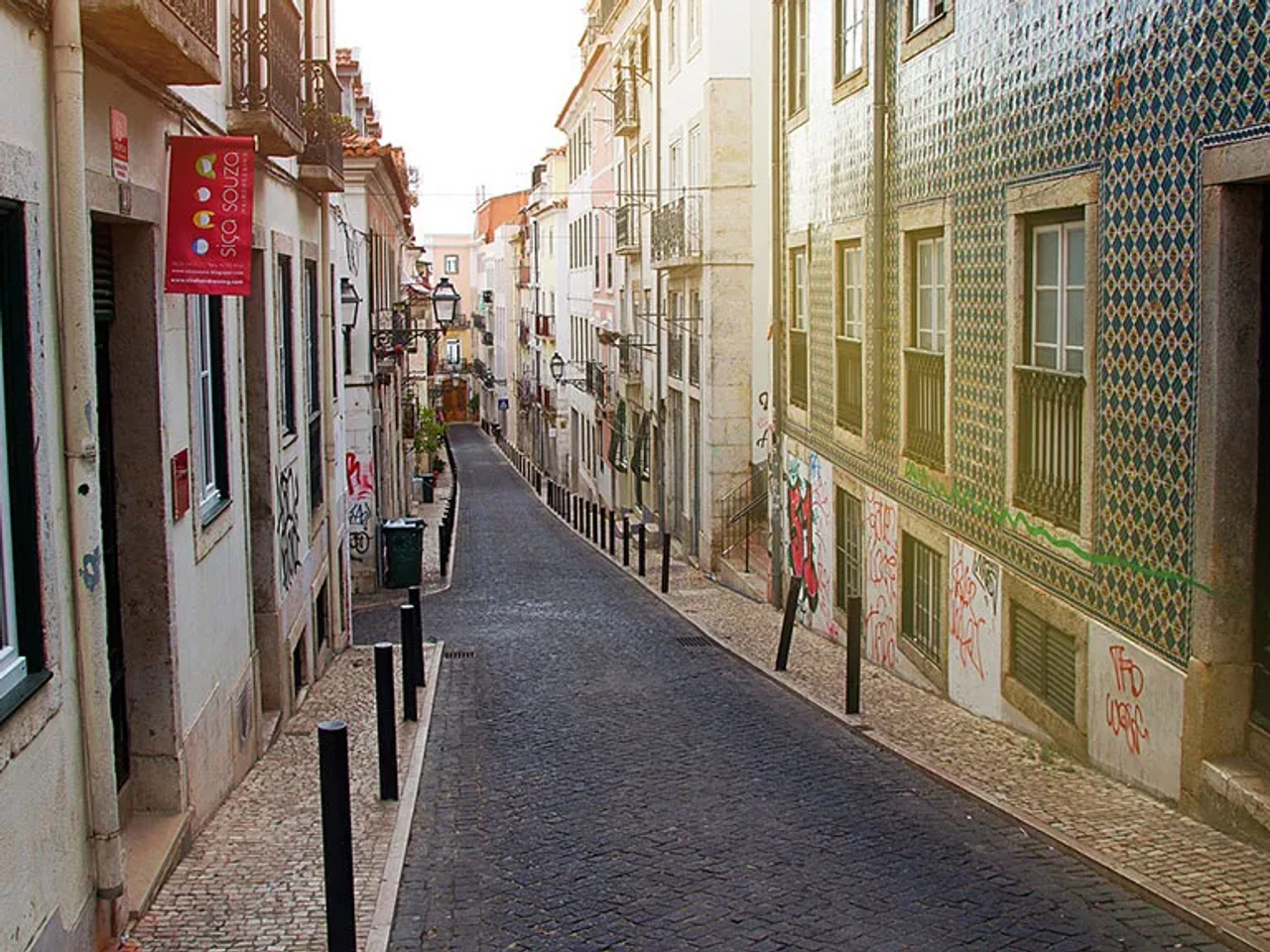 Rua estreita em Lisboa, com fachadas coloridas e azulejos típicos.