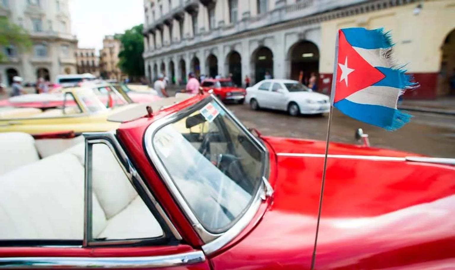 Autos clásicos en Cuba con una bandera cubana en primer plano.