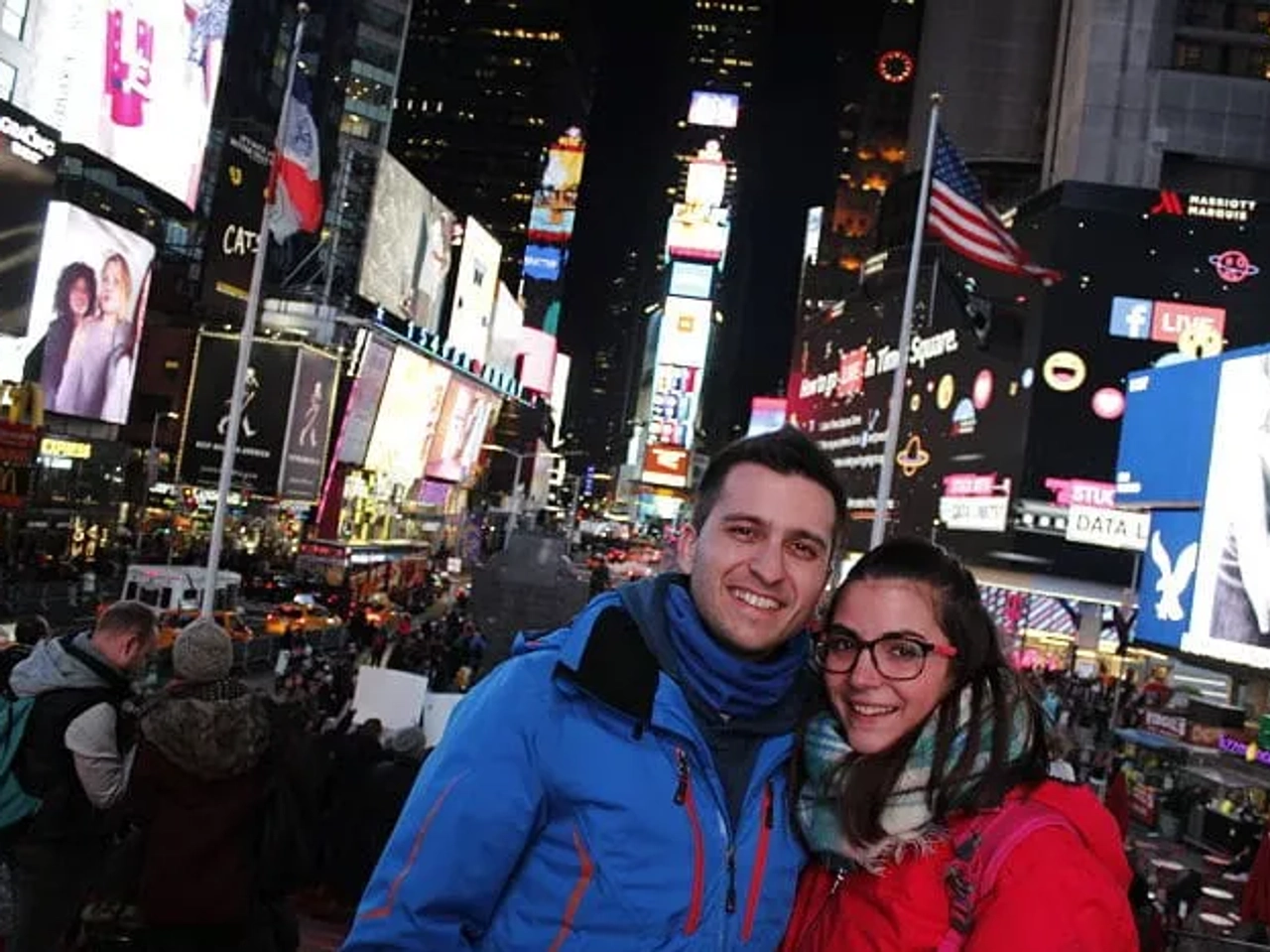 Pareja sonriente en Times Square, rodeada de luces y multitudes.