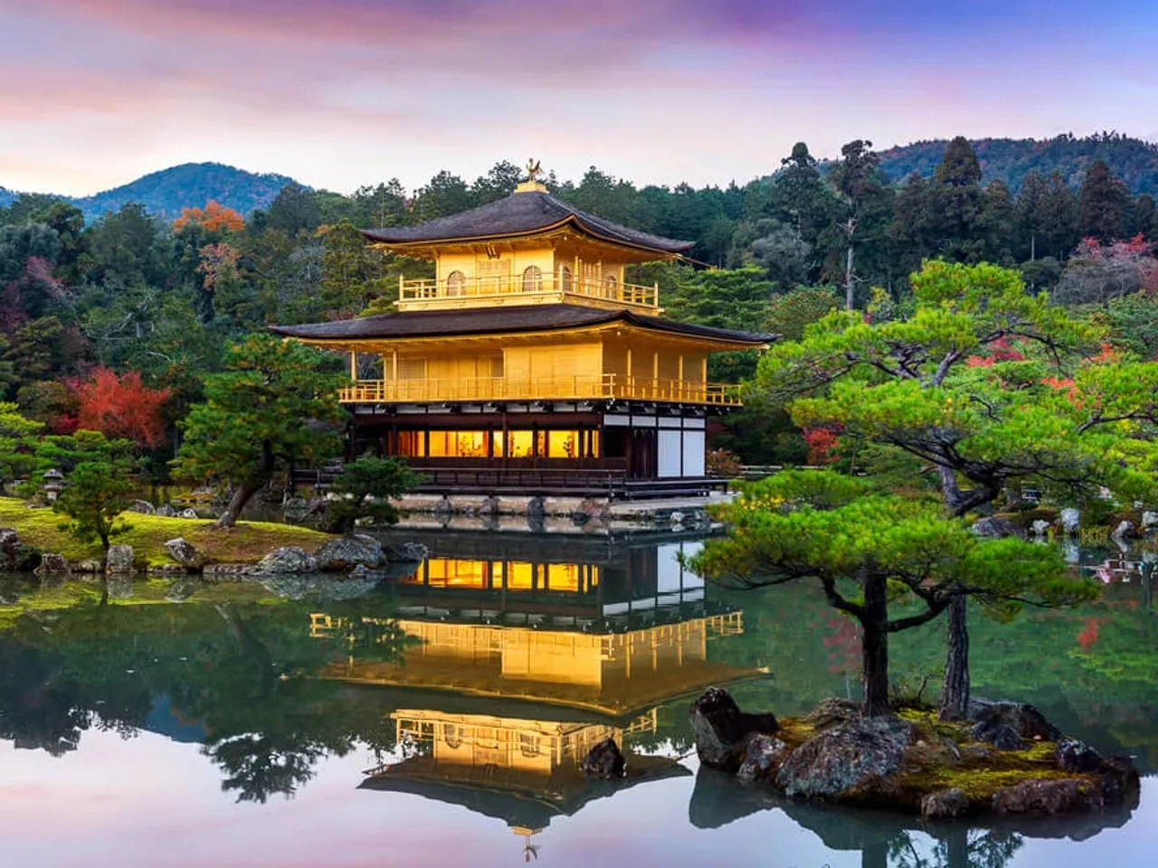 Pavilhão Dourado refletido em lago, cercado por árvores e montanhas.