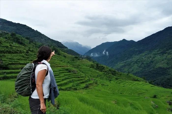 Mujer señalando montañas y campos de arroz en un paisaje verde y montañoso.