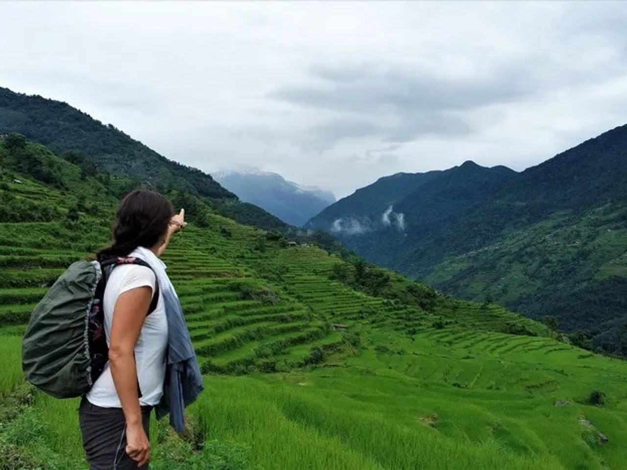 Mujer señalando montañas y campos de arroz en un paisaje verde y montañoso.