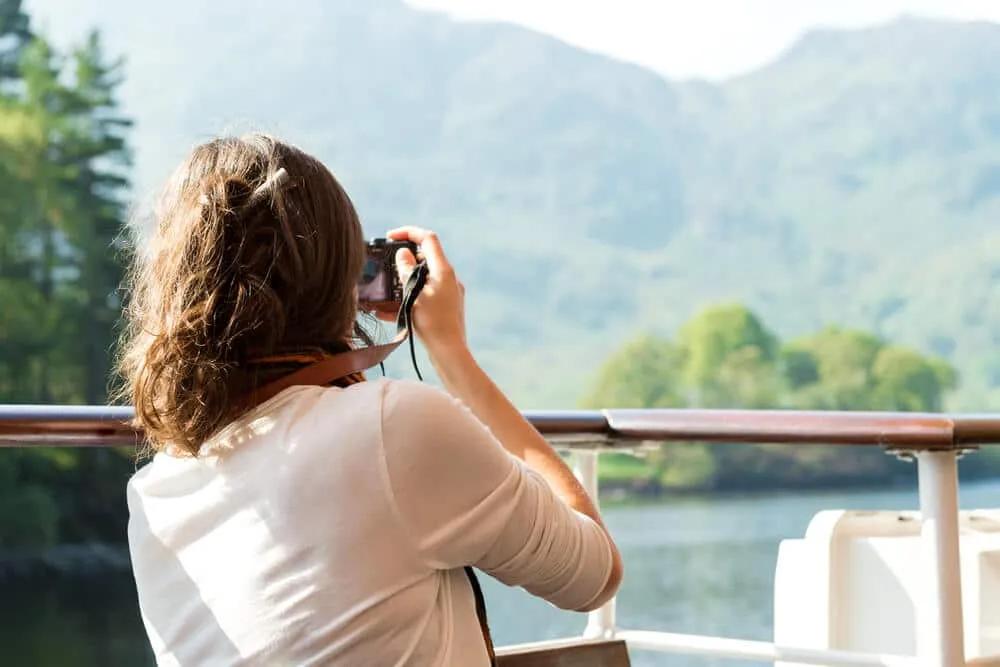 mulher de camisa branca tira fotos desde um barco às montanhas