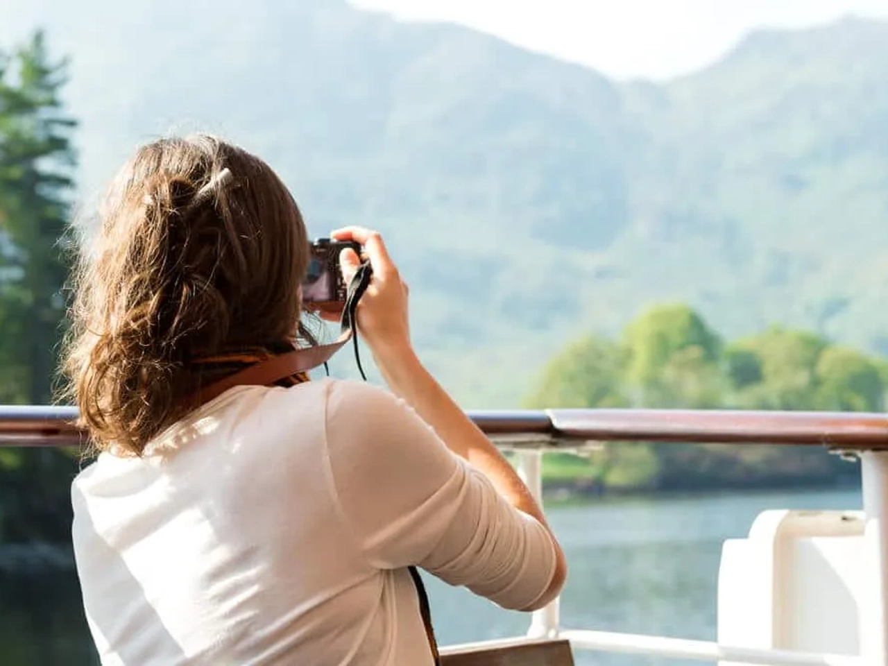 mulher de camisa branca tira fotos desde um barco às montanhas
