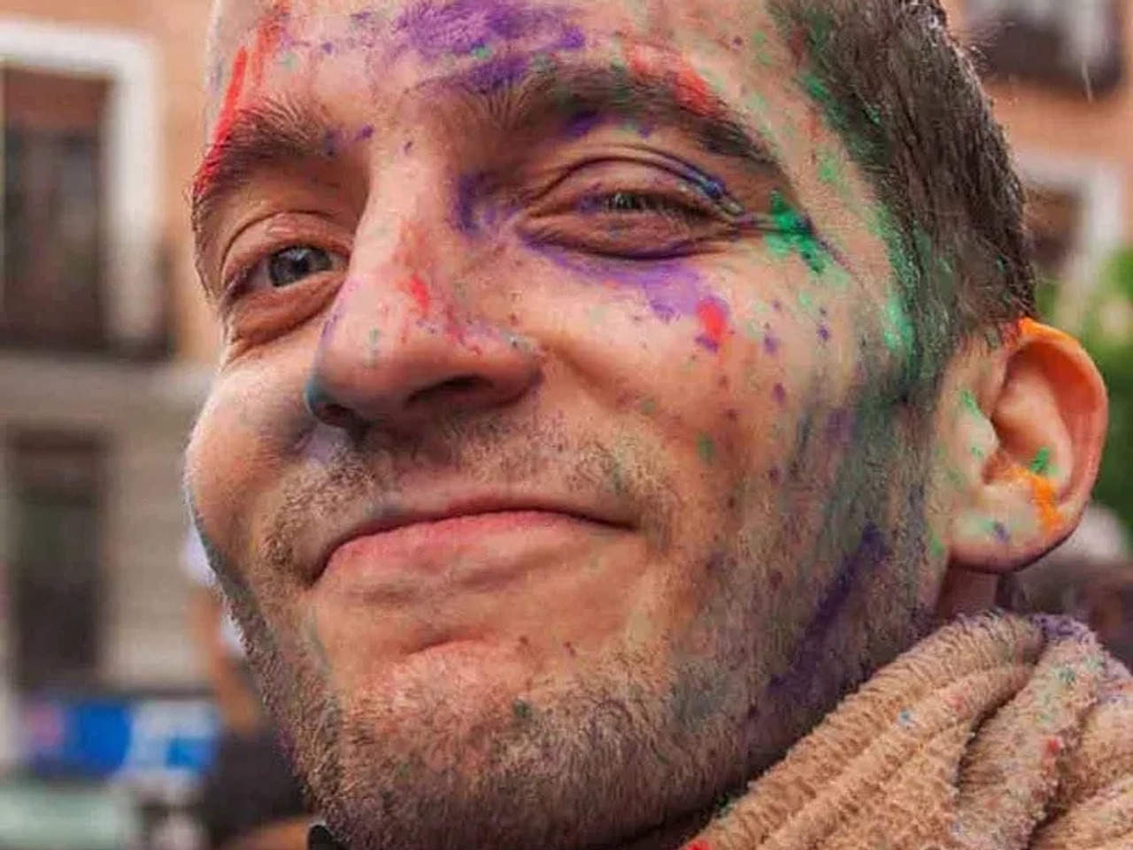 Hombre sonriente con rostro pintado de colores en un ambiente festivo.