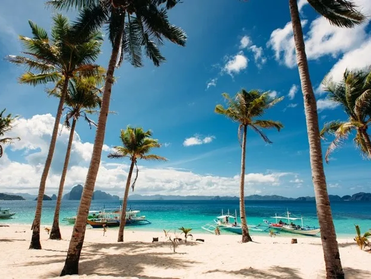 Playa tropical con palmeras y botes en aguas cristalinas de Filipinas.