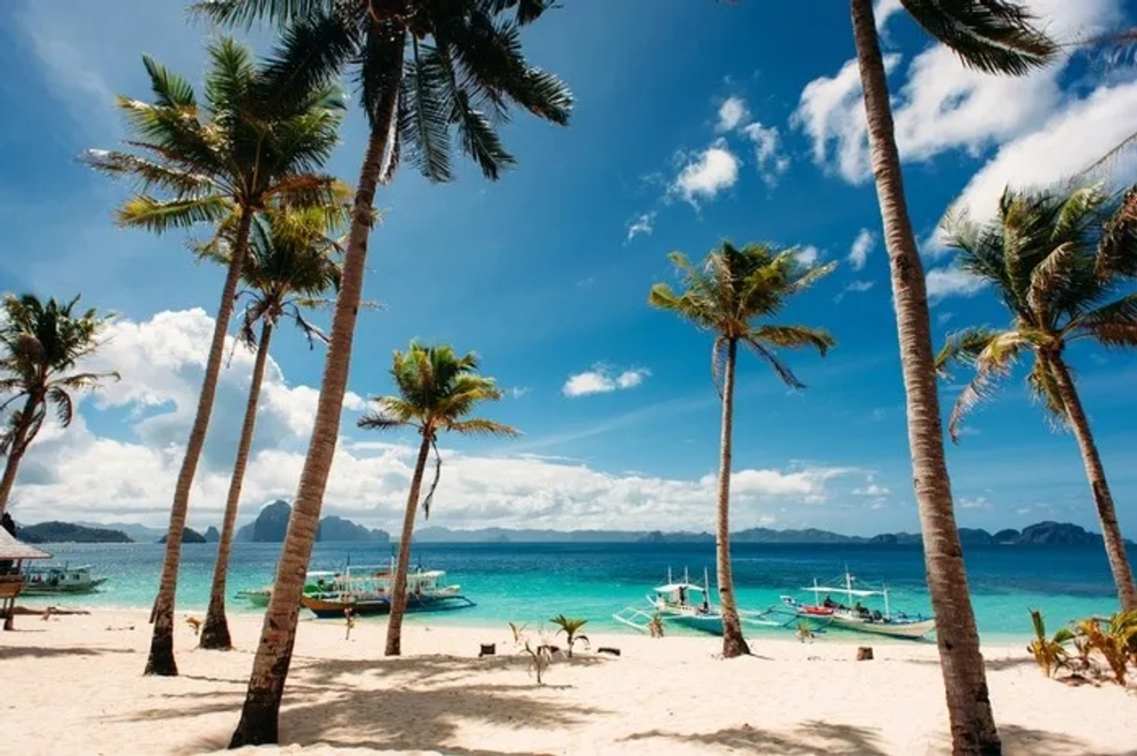 Playa tropical con palmeras y botes en aguas cristalinas de Filipinas.