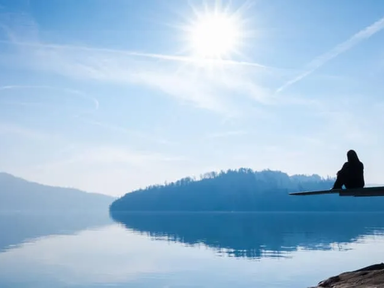 mulher sentada num cais na margem de um lago em posiçao pensativa