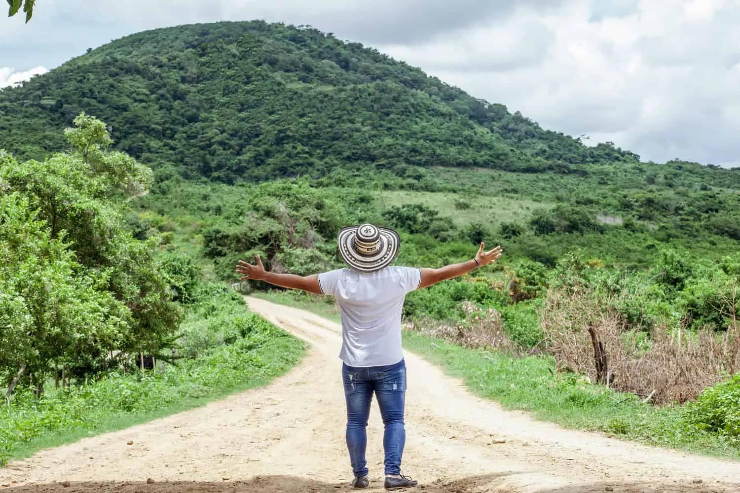 Homem de costas em estrada rural, com montanhas verdes ao fundo.