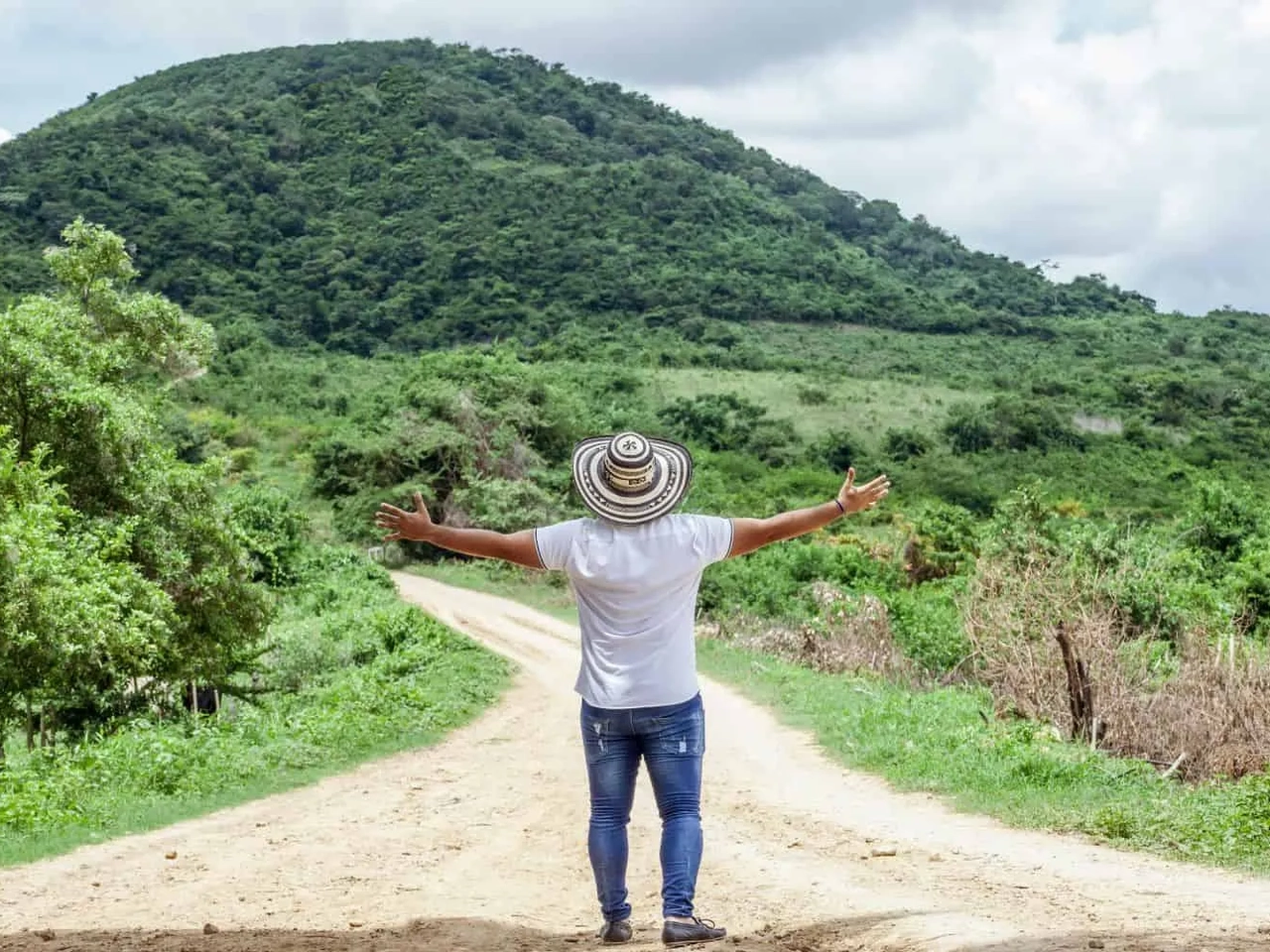 Homem de costas em estrada rural, com montanhas verdes ao fundo.