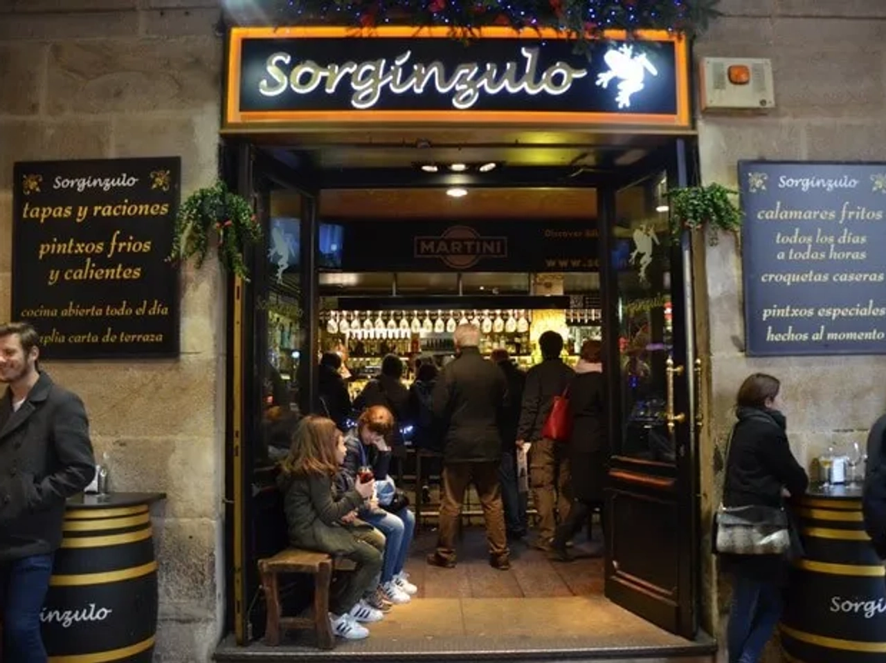 Entrada del bar Sorgingulo, con gente disfrutando pintxos y tapas en Bilbao.
