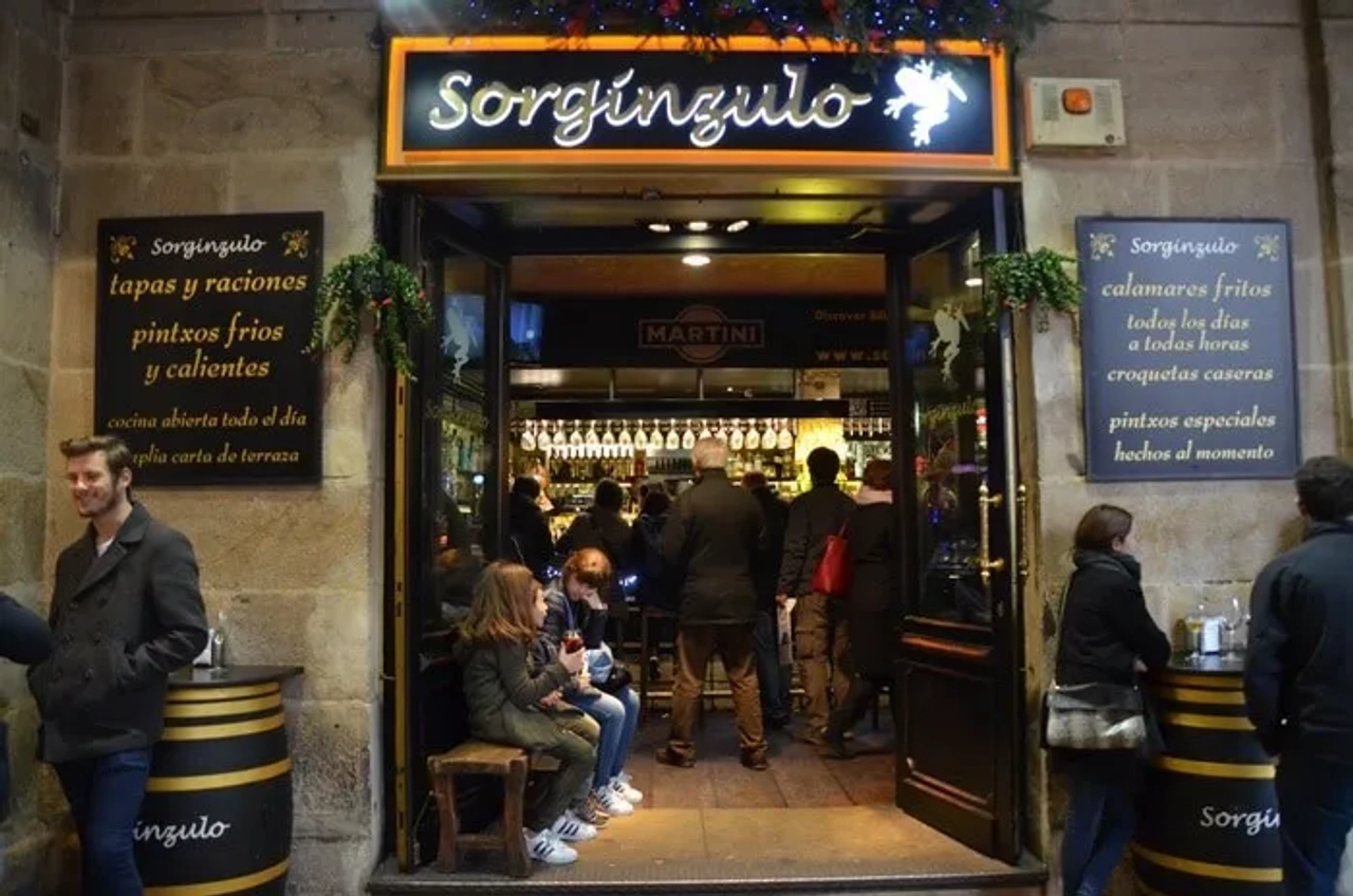 Entrada del bar Sorgingulo, con gente disfrutando pintxos y tapas en Bilbao.