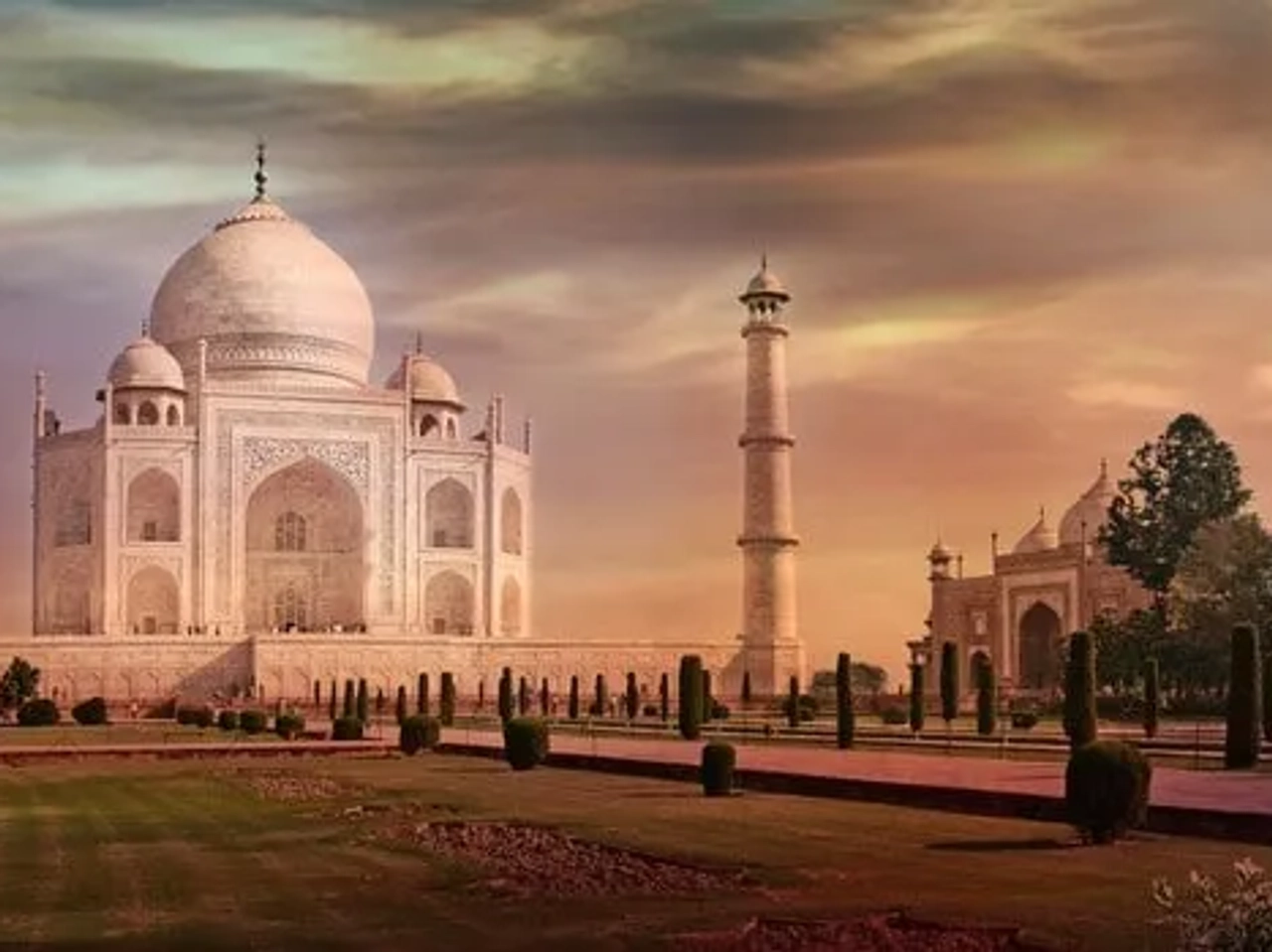 El Taj Mahal al atardecer, rodeado de jardines y torres.