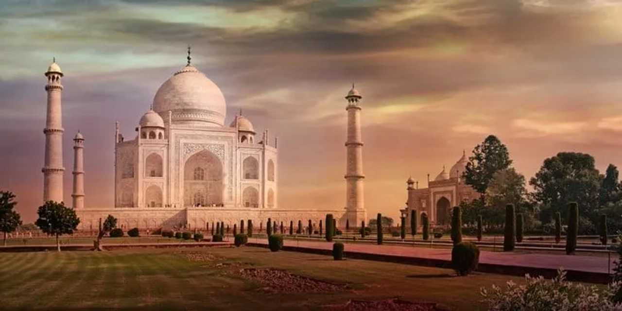El Taj Mahal al atardecer, rodeado de jardines y torres.