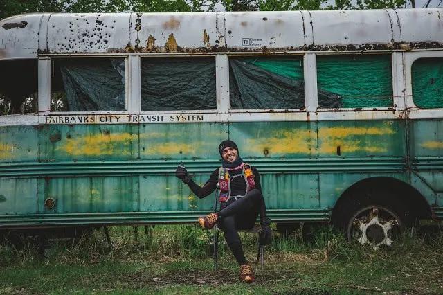 Corredor posando frente a un autobús antiguo en un entorno natural.