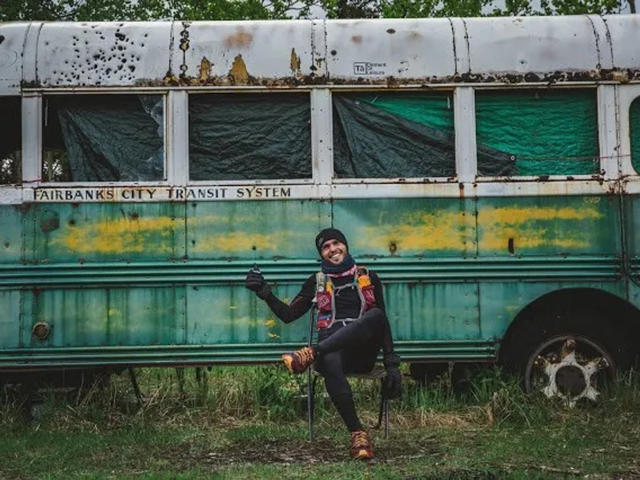 Corredor posando frente a un autobús antiguo en un entorno natural.