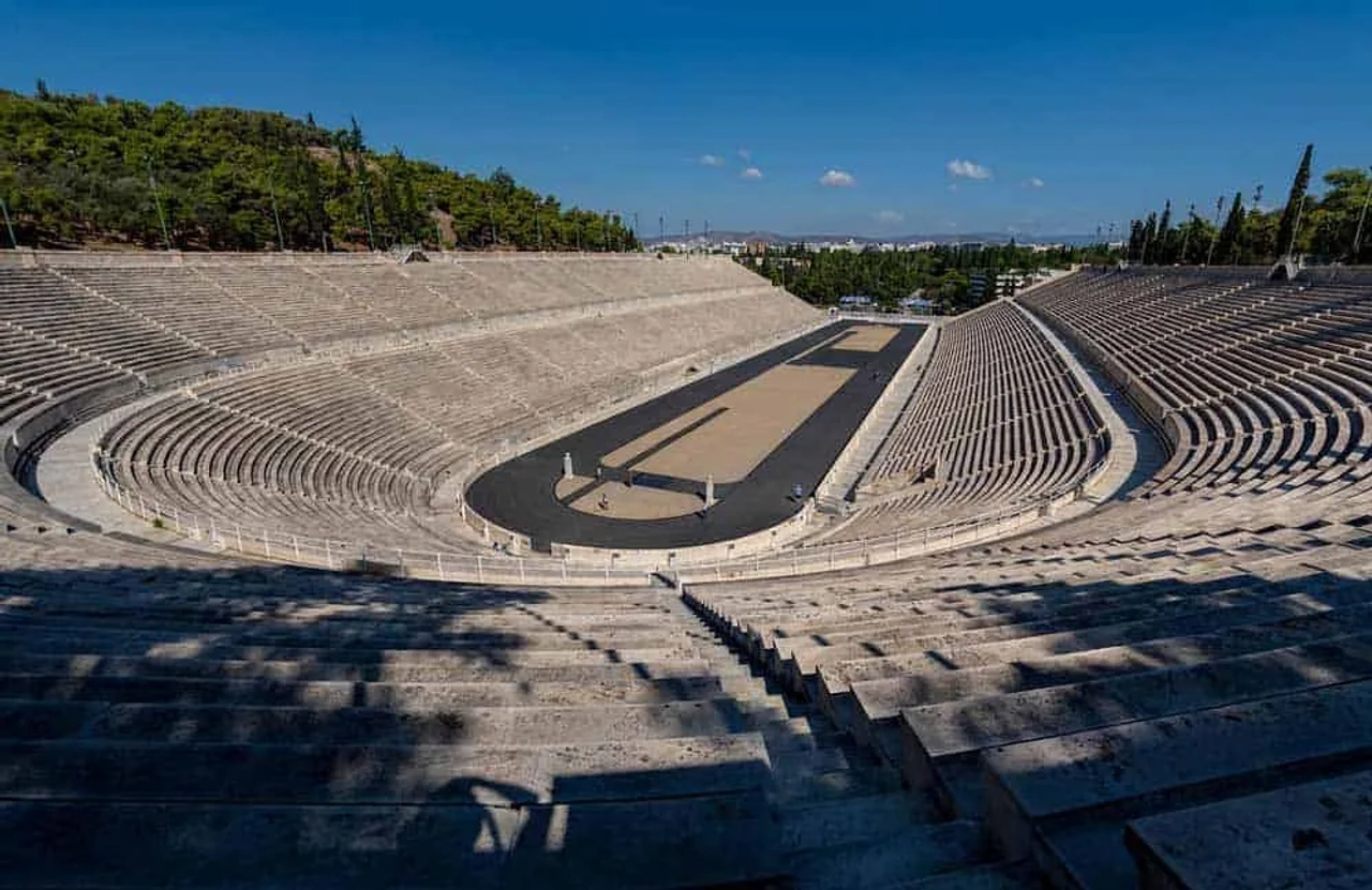 Estádio antigo com arquibancadas de pedra e vista para a natureza ao redor.