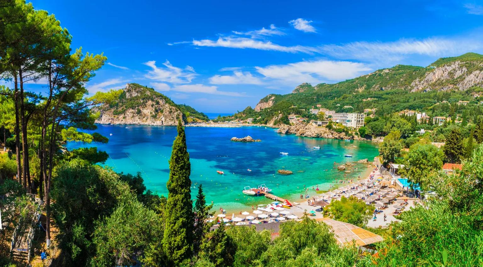 Praia de Corfu com águas cristalinas, vegetação exuberante e áreas de descanso.