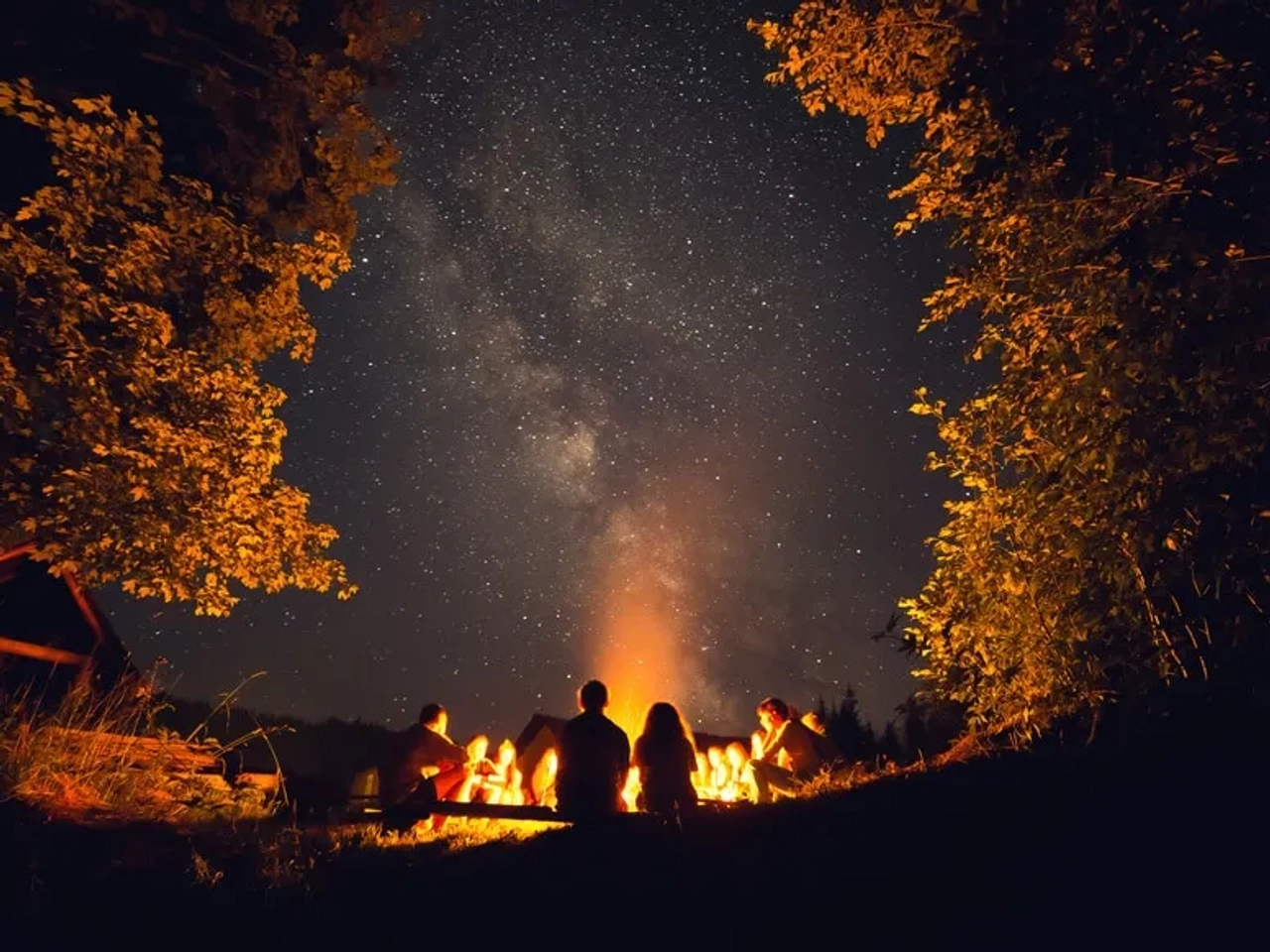 duas pessoas observam a via lactea desde à volta de uma fogueira