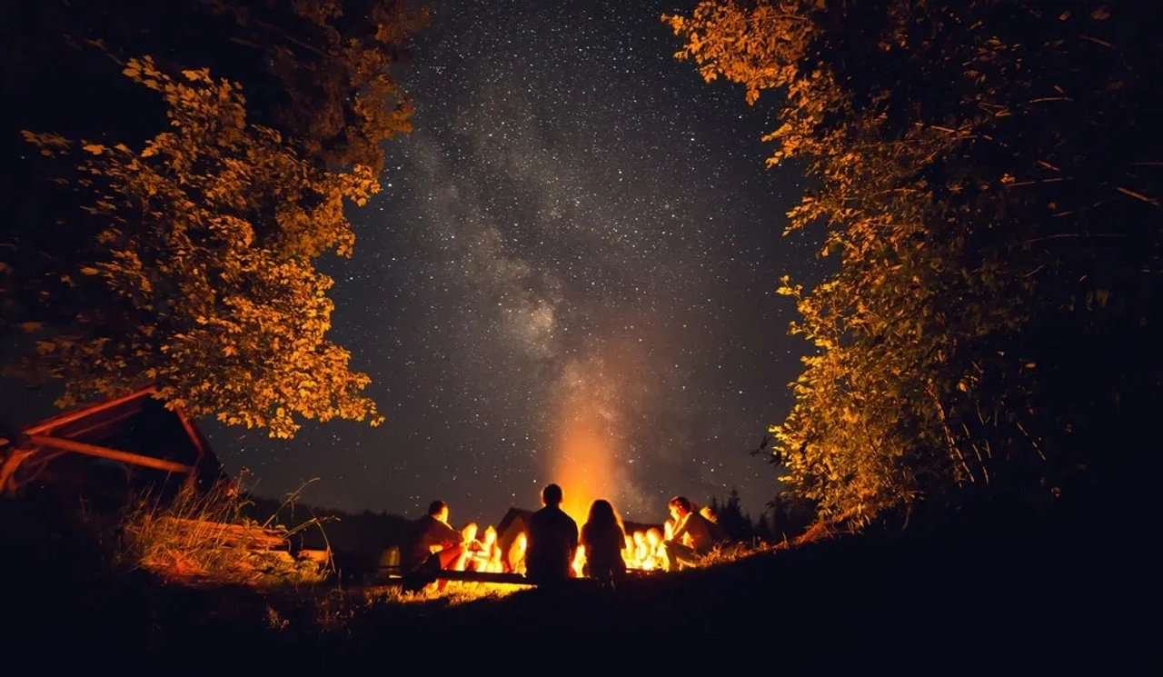 duas pessoas observam a via lactea desde à volta de uma fogueira
