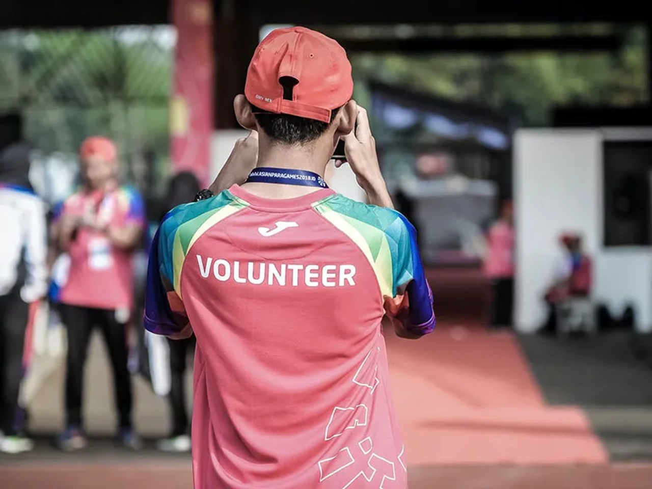 Pessoa com camiseta de voluntário, tirando foto em evento. Ambiente de trabalho colaborativo.