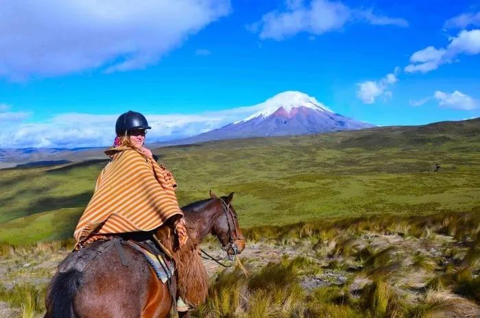 Persona montando a caballo con un paisaje montañoso y cielo azul de fondo.