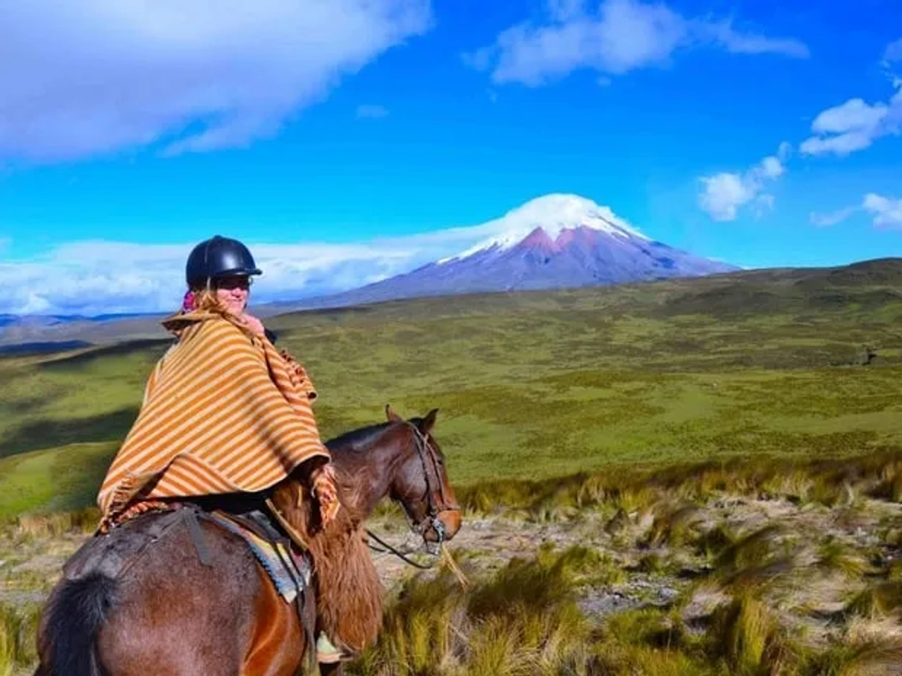 Persona montando a caballo con un paisaje montañoso y cielo azul de fondo.