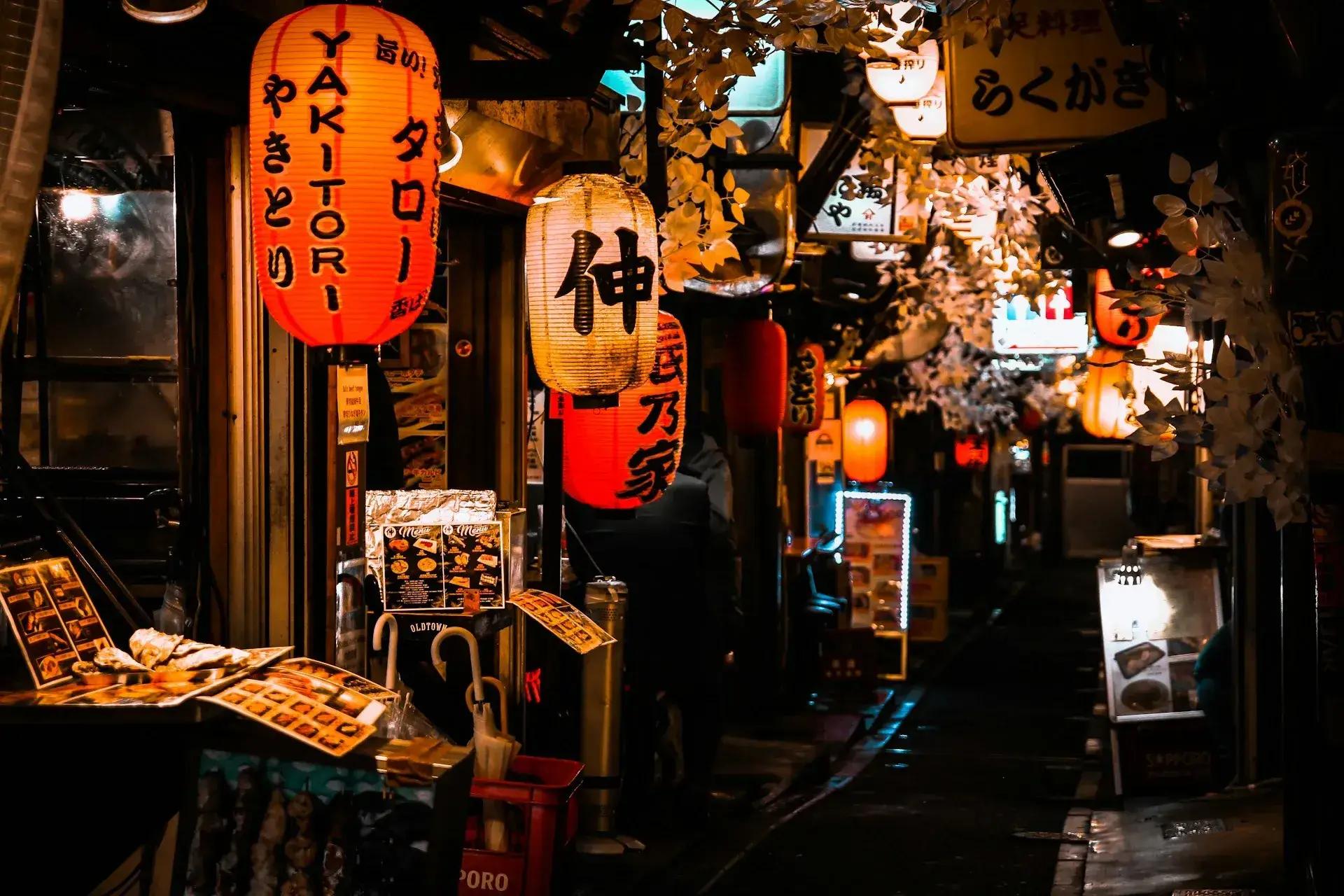 Vicolo di Tokyo illuminato di notte, con lanterne giapponesi, insegne dei ristoranti e piccoli locali tradizionali lungo la strada.