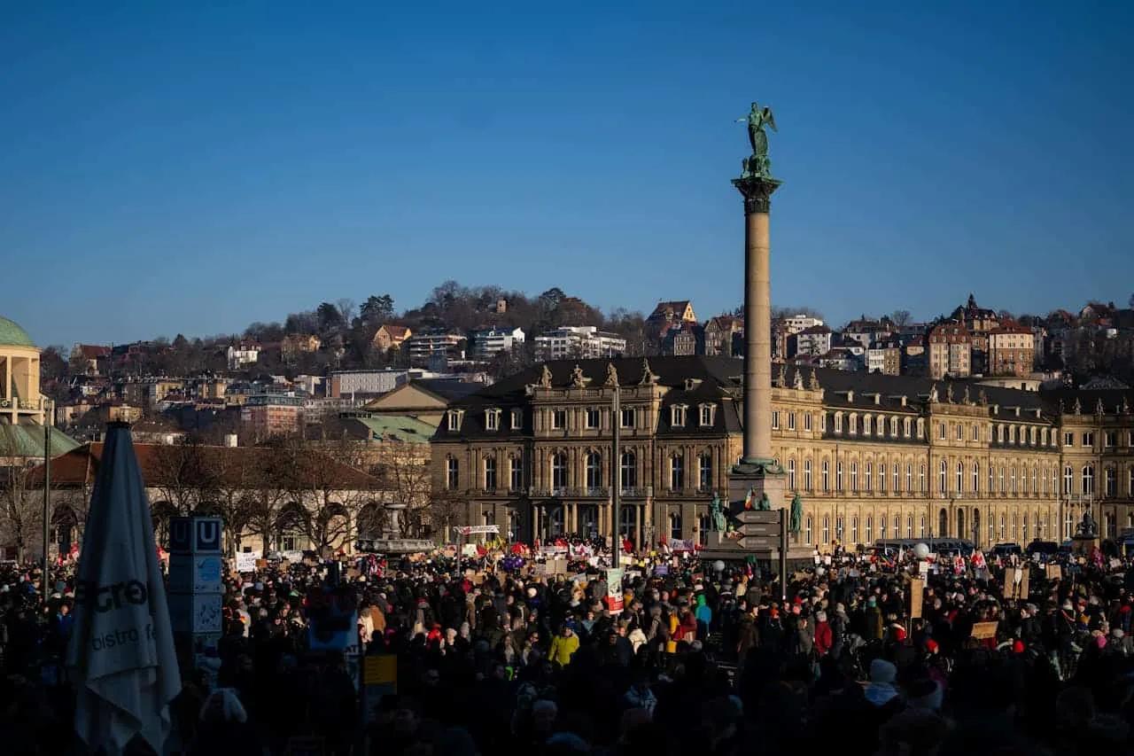 Praça movimentada em Stuttgart, com monumento e edifícios históricos ao fundo.