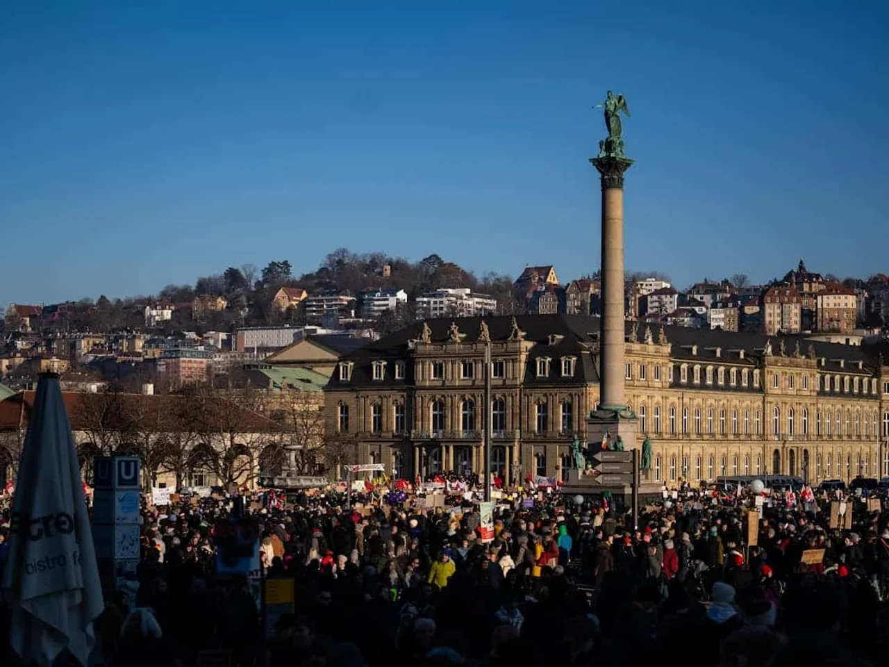 Praça movimentada em Stuttgart, com monumento e edifícios históricos ao fundo.