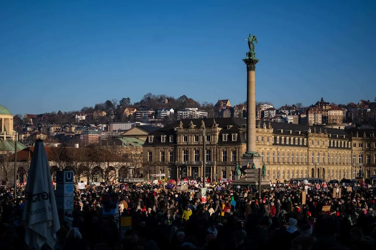 Praça movimentada em Stuttgart, com monumento e edifícios históricos ao fundo.