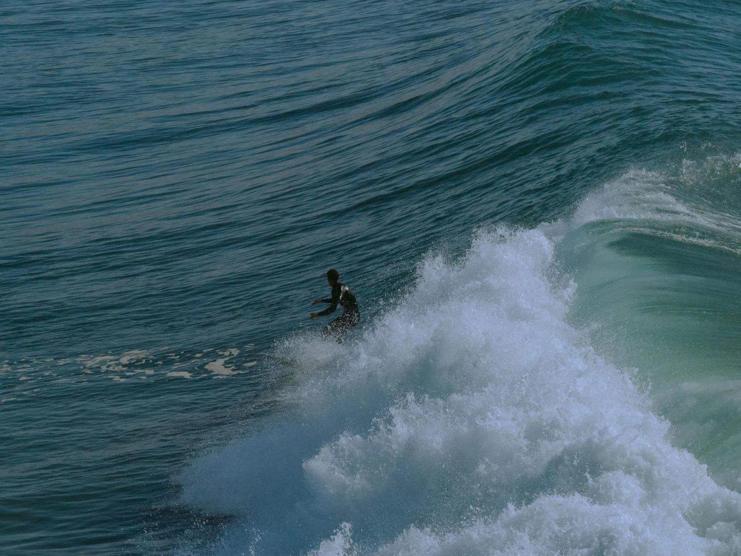 Surfista pegando onda em uma praia de Marrocos. Água azul e ondas grandes.