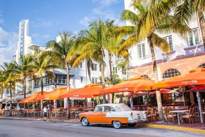Calle de Miami con palmeras, restaurantes al aire libre y un auto clásico.