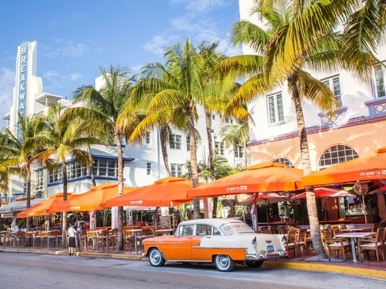 Calle de Miami con palmeras, restaurantes al aire libre y un auto clásico.