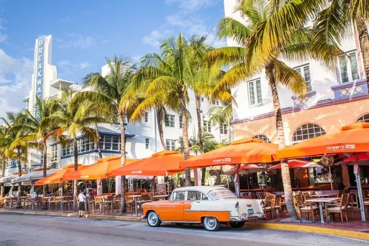 Calle de Miami con palmeras, restaurantes al aire libre y un auto clásico.