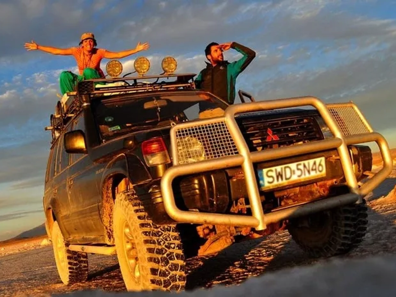 Dos personas sobre un vehículo todoterreno en un paisaje desértico al atardecer.