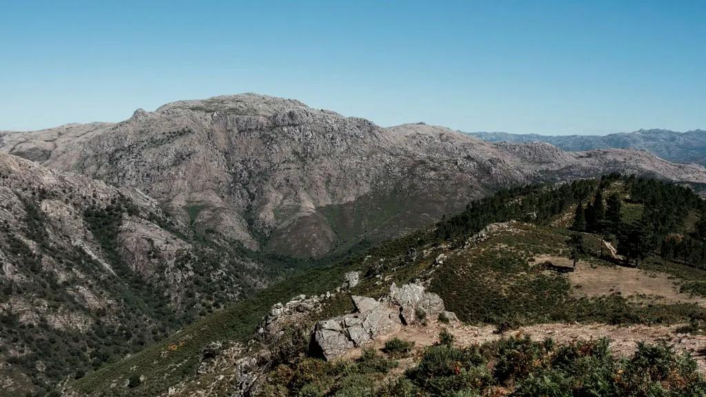 Paisagem montanhosa com vegetação densa e céu claro, ideal para campismo.