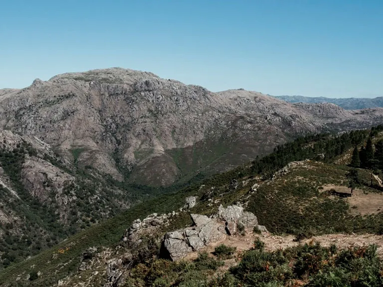 Paisagem montanhosa com vegetação densa e céu claro, ideal para campismo.
