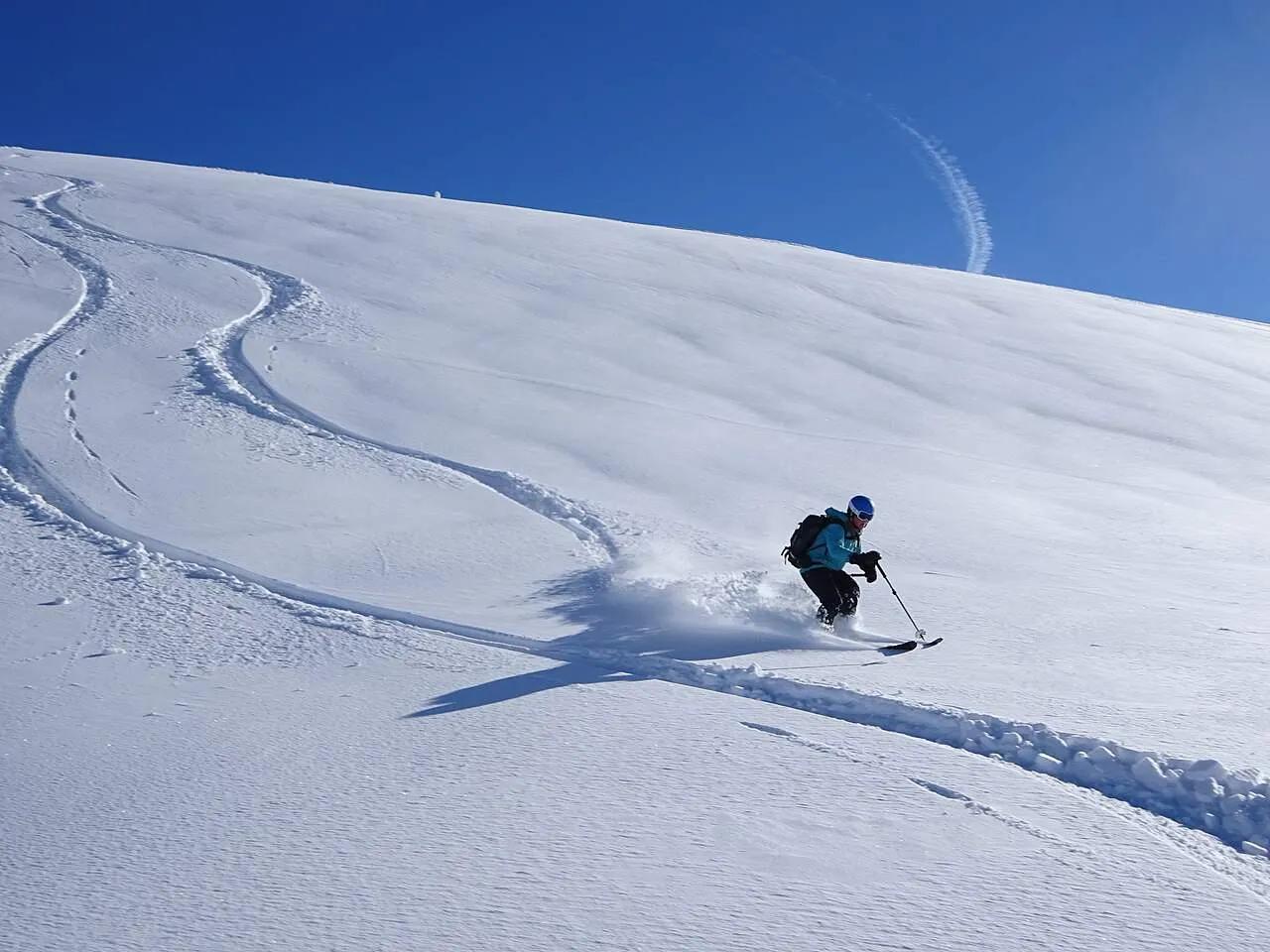 Esquiador descendo uma pista de neve sob um céu azul claro.
