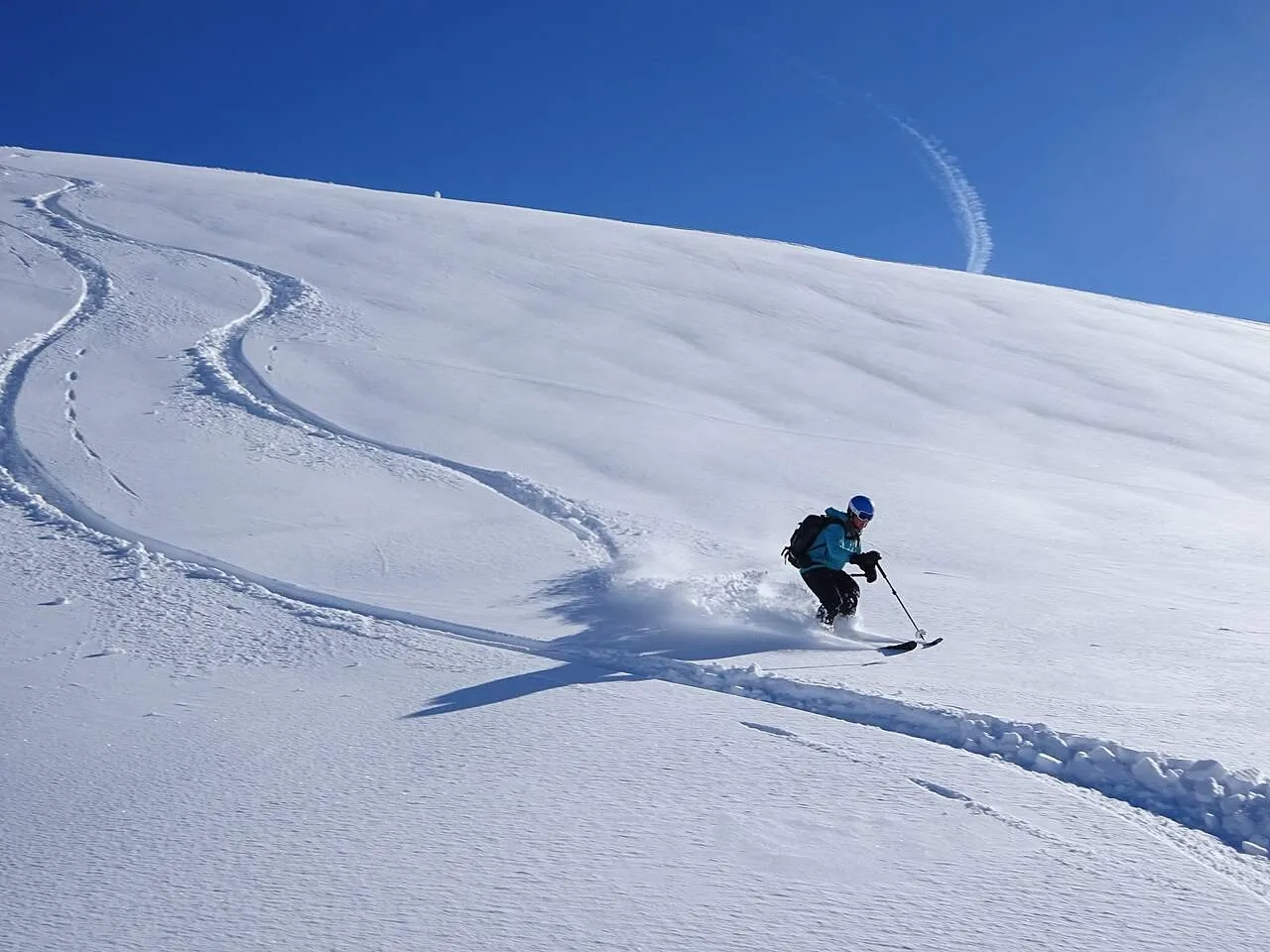 Esquiador descendo uma pista de neve sob um céu azul claro.