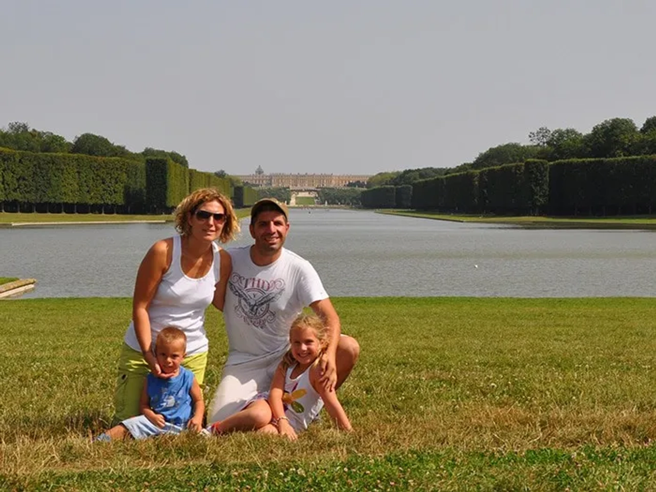 Familia sonriente posando frente a un lago y jardines.