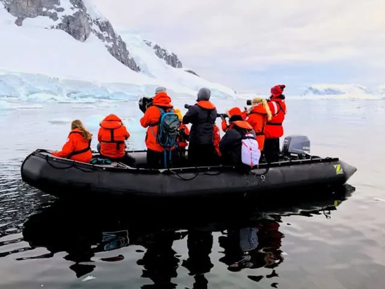 pessoas a andar num barco a motor com casacos vermelhos e camaras fotograficas a observar a vida selvagem da antartida