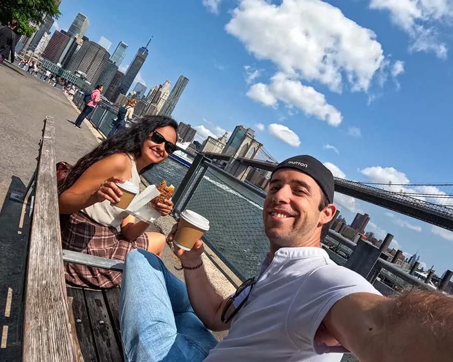 Pareja disfrutando de café y comida con vista a la ciudad y el puente.