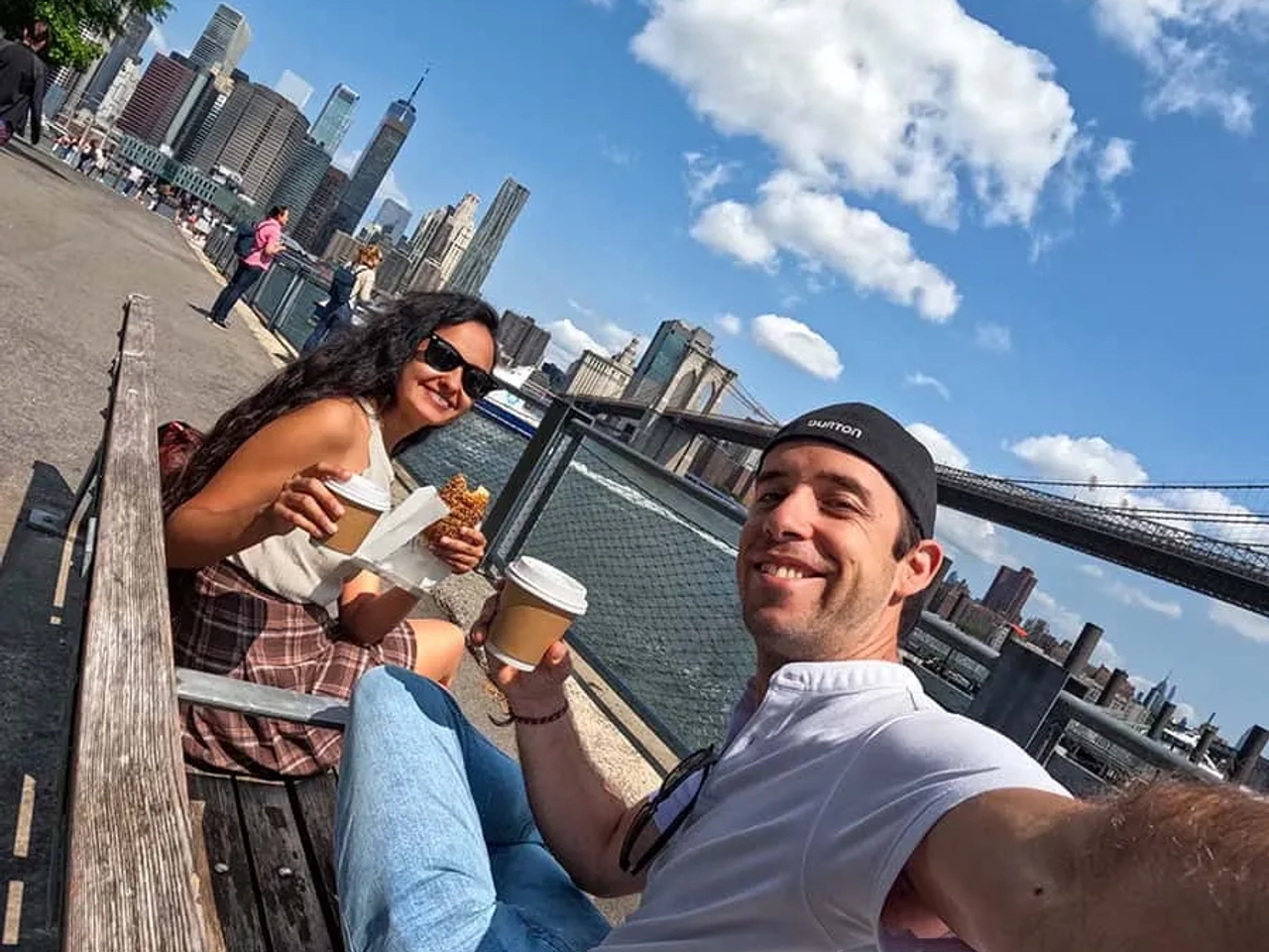 Pareja disfrutando de café y comida con vista a la ciudad y el puente.