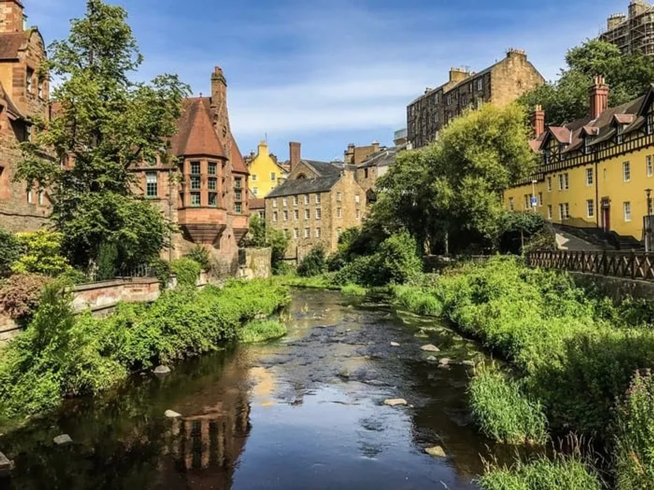 Vista de um rio cercado por edifícios históricos e vegetação em Edimburgo.