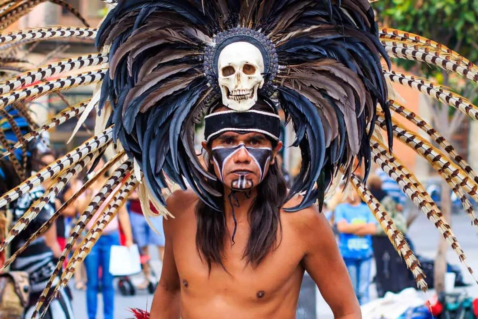Hombre con atuendo tradicional y plumas en un carnaval mexicano.