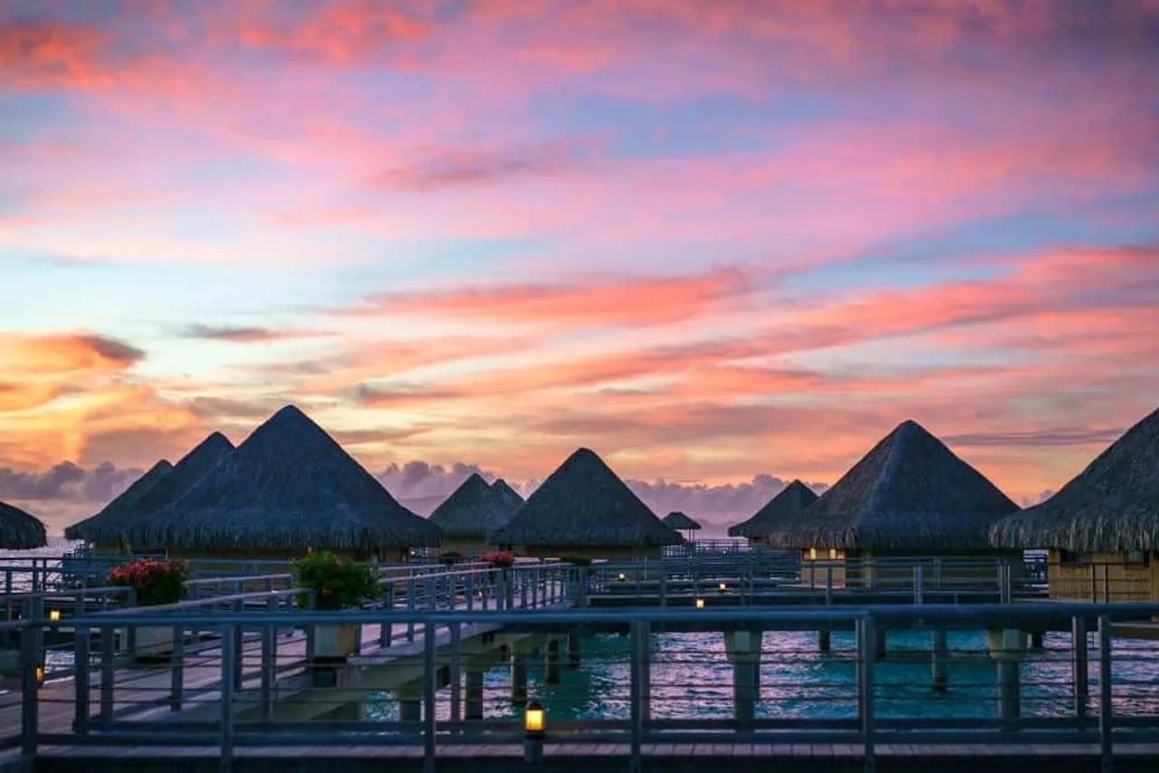 Atardecer sobre bungalows de palapa en la Polinesia Francesa.